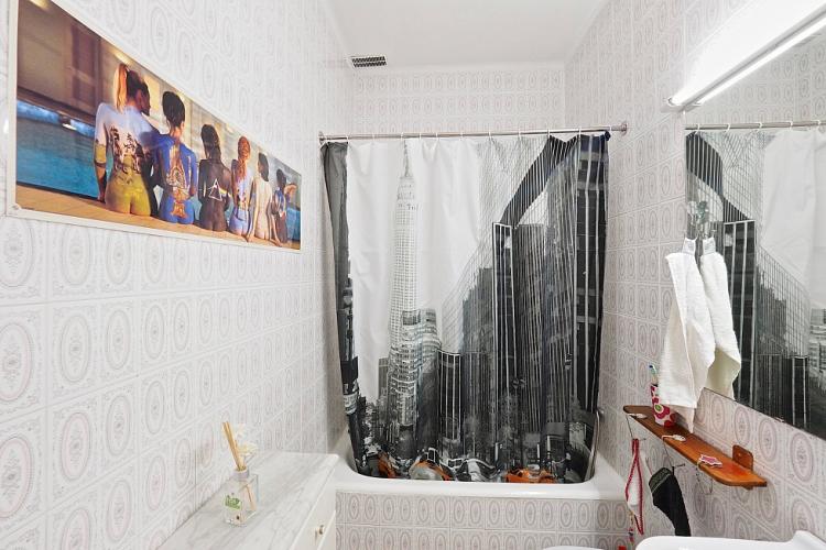 This bathroom is decorated with a black and white New York sky scraper themed shower curtains and a Pink Floyd poster on the wall.